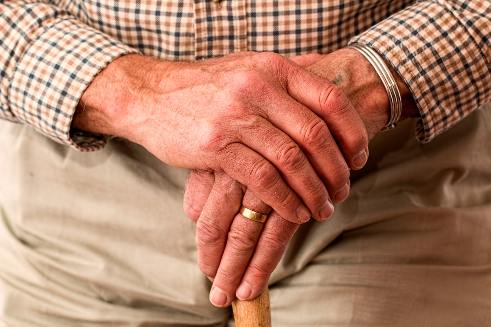Ein älterer Mensch stützt die Hände auf einen Gehstock.
